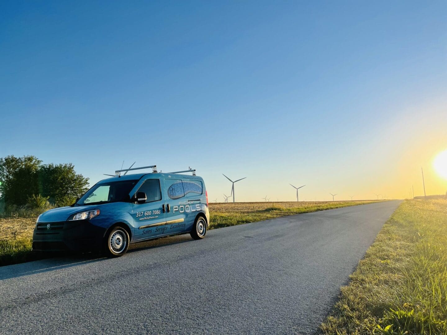 A van is driving down the road near some wind mills.