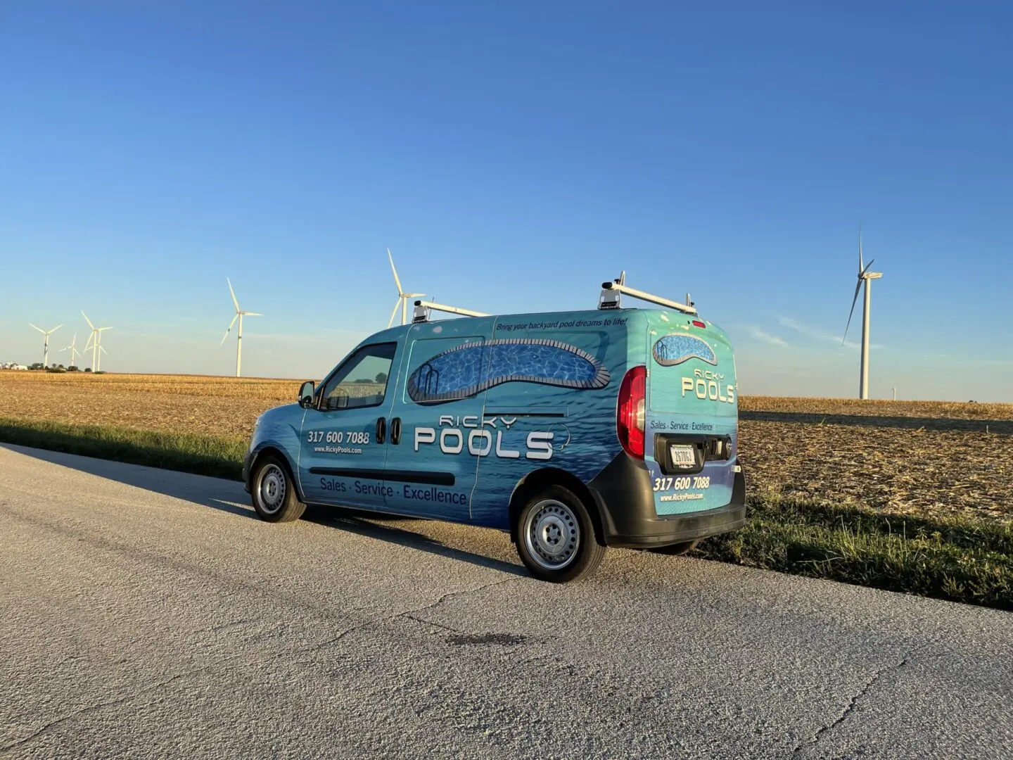 A van parked on the side of a road near some wind mills.